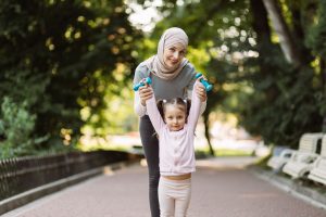 Sporty fit Arab woman showing her little kid working out with dumbbells
